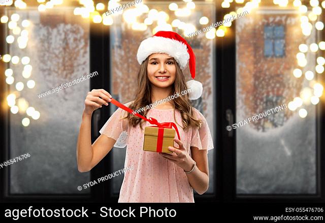 teenage girl in santa hat opening christmas gift