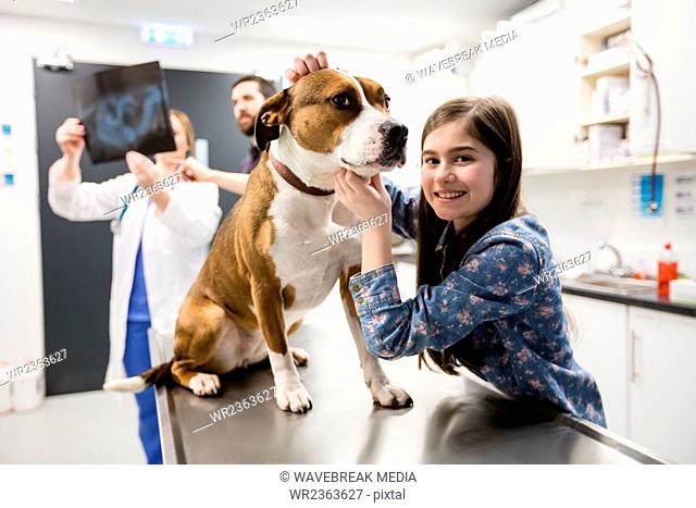 Girl playing with her pet dog while vet discussing x-ray in background