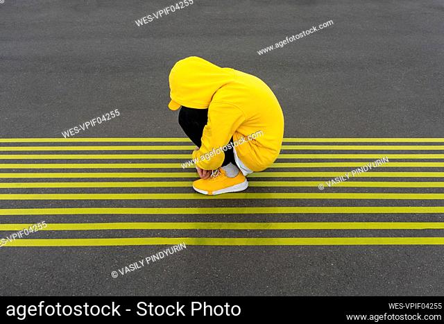 Depressed boy crouching on striped yellow road markings