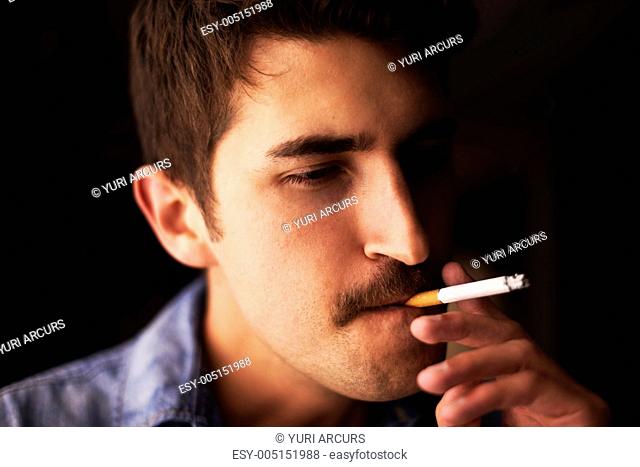 Closeup of a young guy with a moustache dragging on a cigarette