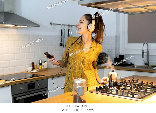 Young woman listening musuc in the kitchen, while preparing her morning coffee