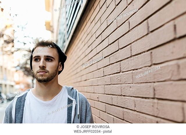Young man walking in the city next to a wall
