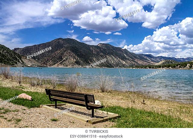 Metal sitting bench near shoreline of mountain lake on sunny summer afternoon
