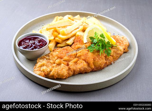 Fried Wiener schnitzel from veal topside with French fries and cranberry sauce as closeup modern design plate