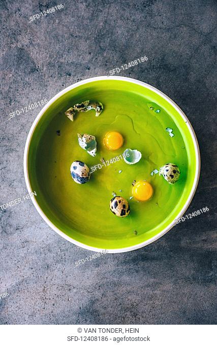 Whole and cracked quail eggs in a green bowl