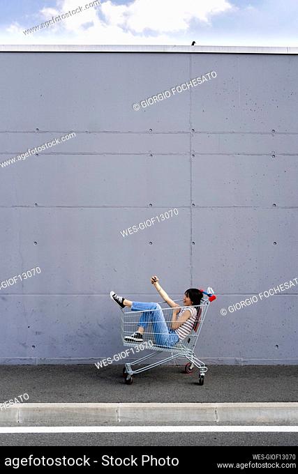 Young woman taking selfie on mobile phone while sitting in shopping cart