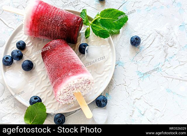Homemade vegan berry popsicles with coconut milk, fresh blueberries and green mint on a white concrete table
