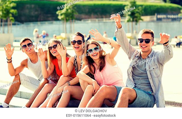 friendship, leisure, summer, gesture and people concept - group of laughing friends sitting on city square
