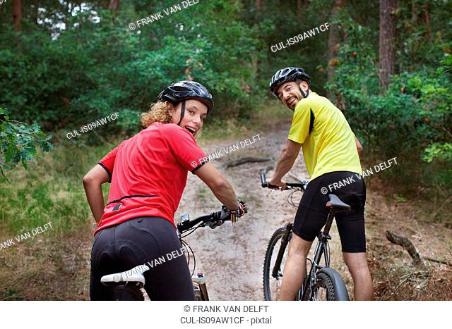 Portrait of mountain biking couple looking over their shoulders in forest