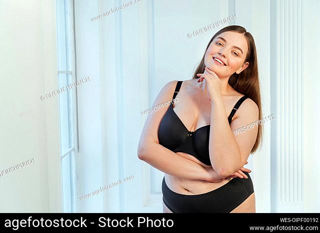 Curvy young woman wearing bra and jeans standing against white
