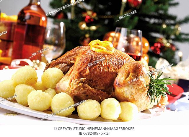 Roast turkey on a festive table setting served with dumplings in front of a decorated Christmas tree