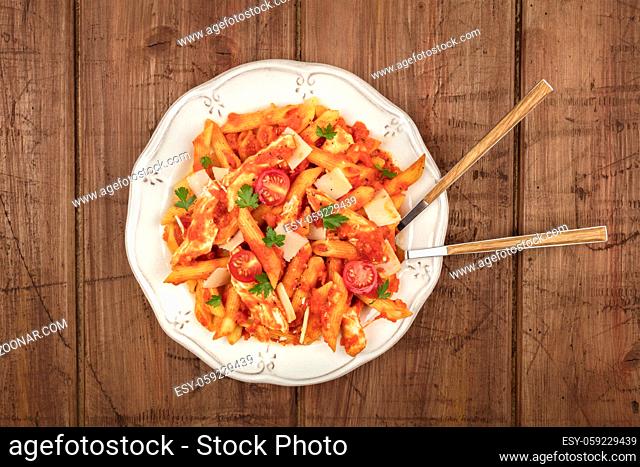 An overhead photo of a plate of penne pasta with chicken and tomato sauce, with a fork and a spoon plunged into the dish