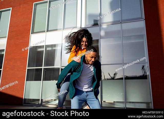 Man giving piggyback to girlfriend against glass building