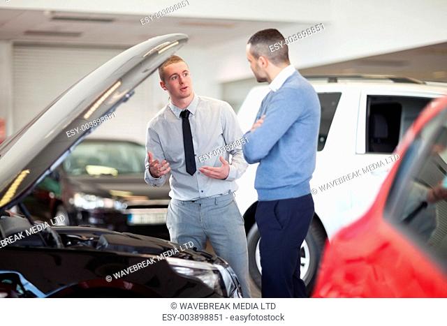 Two men chatting in front of an open engine in a car dealership