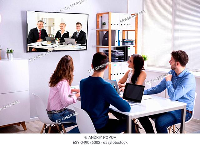 Rear View Of Businesspeople Attending Videoconference Meeting In Office