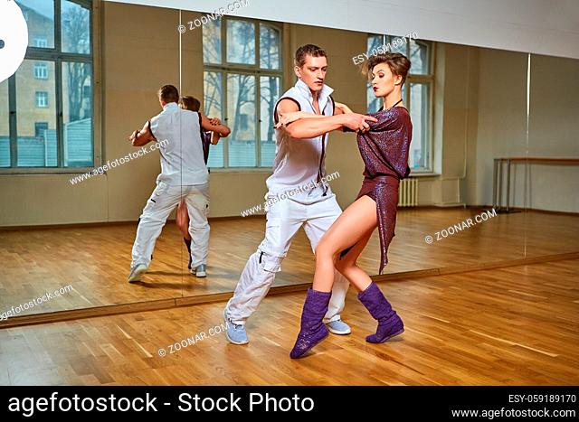beautiful young couple dancing bachata in dance studio mirror room. woman in purple dress and man in white suit. copy space