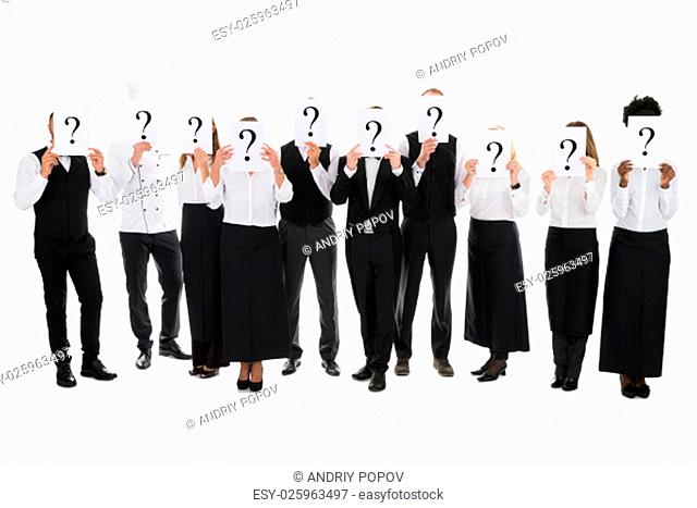 Full length of restaurant staff hiding faces with question mark signs against white background