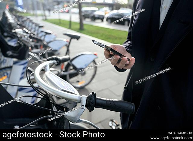 Businessman paying through smart phone at bicycle parking station