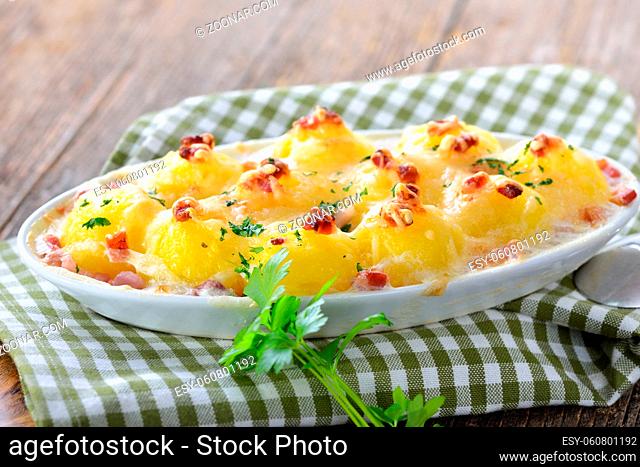 Deftige Kartoffelnocken in Sahnesoße mit Speck und Käse überbacken und frisch aus dem Ofen serviert - Hearty potato dumplings baked with cheese and bacon