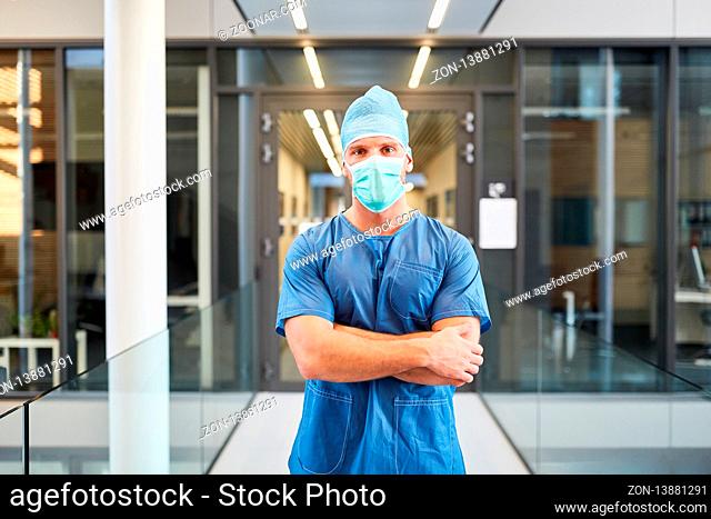 Junger Mann als Chirurg mit verschränkten Armen vor der Notaufnahme in der Klinik
