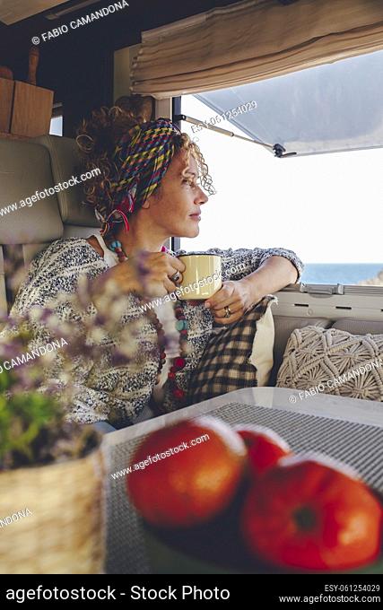Serene adult woman admiring outdoors destination sitting inside her modern camper van and enjoying a coffee. Independent traveler tourist female people with...