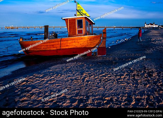 22 March 2021, Mecklenburg-Western Pomerania, Ahlbeck: A wooden fishing boat lies on the beach in front of the Ahlbeck pier
