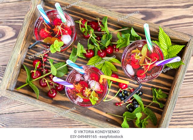 Three glasses of refreshing drink flavored with fresh fruit in wooden box surrounded by fruit. Top view. Wooden background