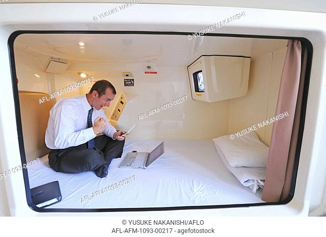 Businessman sitting in pod of capsule hotel