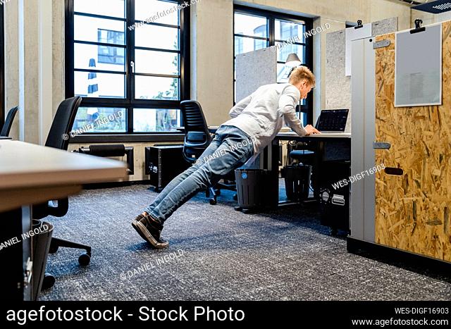Young businessman doing push-ups at workplace