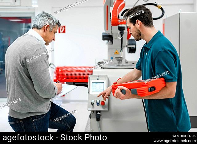 Young male engineer holding control while operating machine by mature entrepreneur in industry