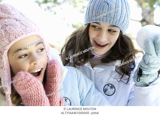 Two teenage girls smiling, one holding up snowball, both dressed in winter clothing