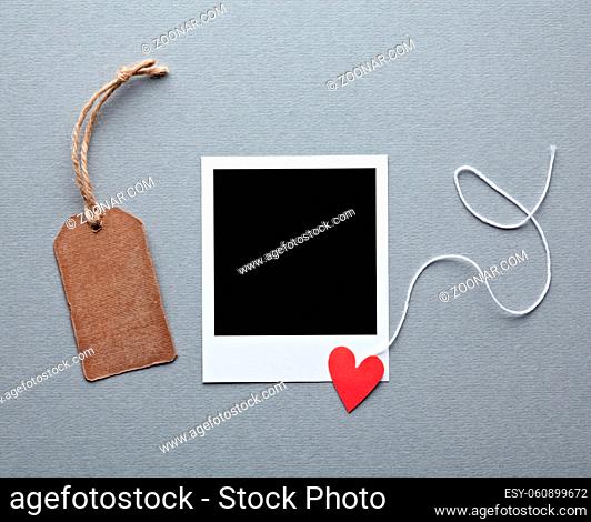 Instant photo frame with blank gift tag and small red heart. On gray paper background