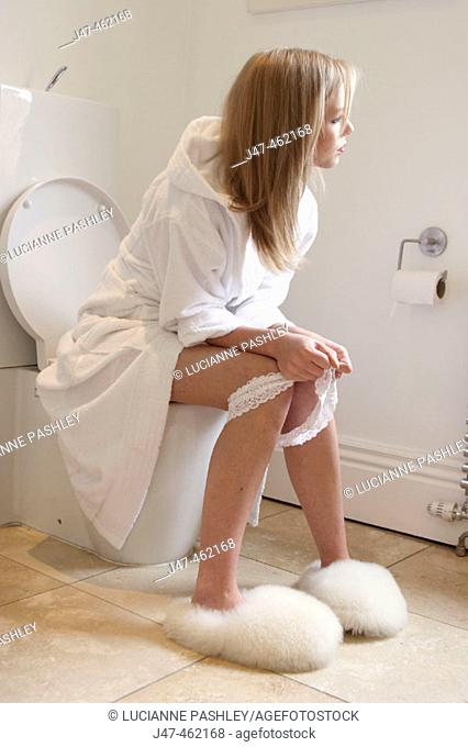 Girl sitting on the toilet with pants round her ankles