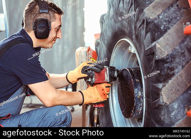 Farm machine mechanic working on wheel with power tool