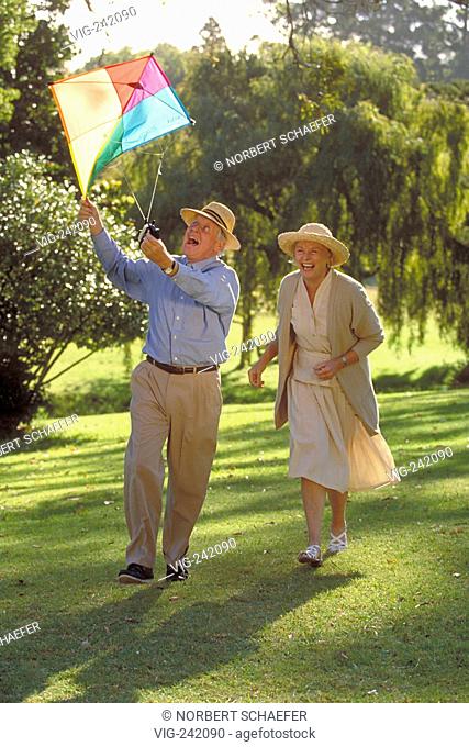 park-scene, full-figure, senior-couple wearing bright dresses and strawhats runs over a meadow and lets a coloured kite fly  - GERMANY, 23/08/2004