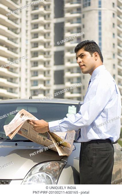 Businessman reading a newspaper beside a car, Gurgaon, Haryana, India