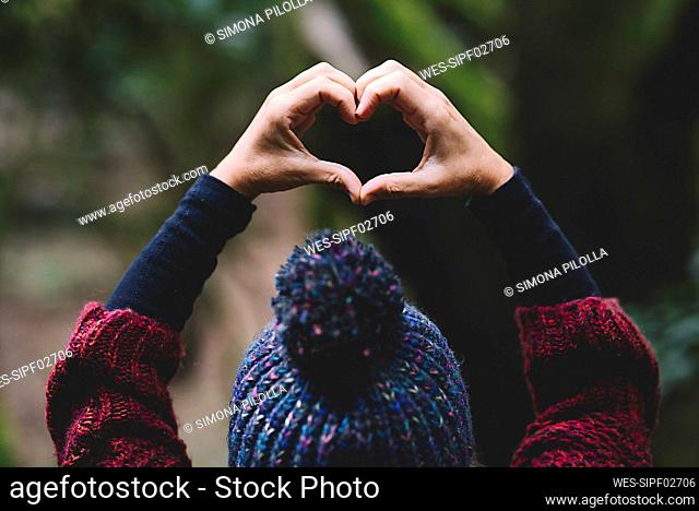 Woman making heart sign with hands in forest