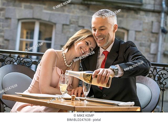 Well-dressed Caucasian man pouring champagne for woman