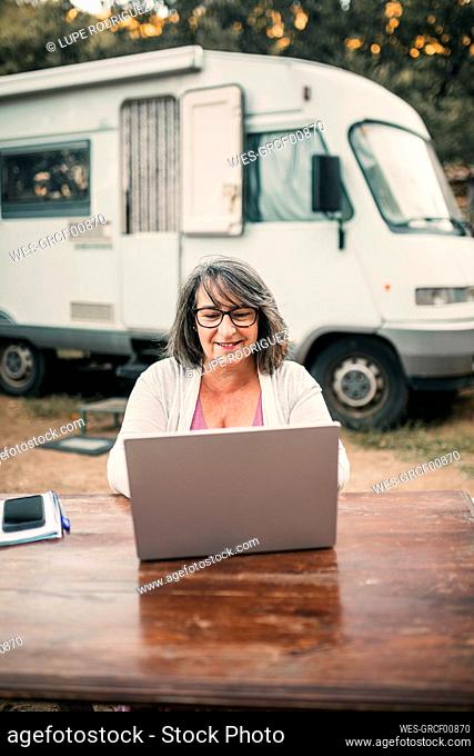 Smiling mature woman using laptop while sitting at table