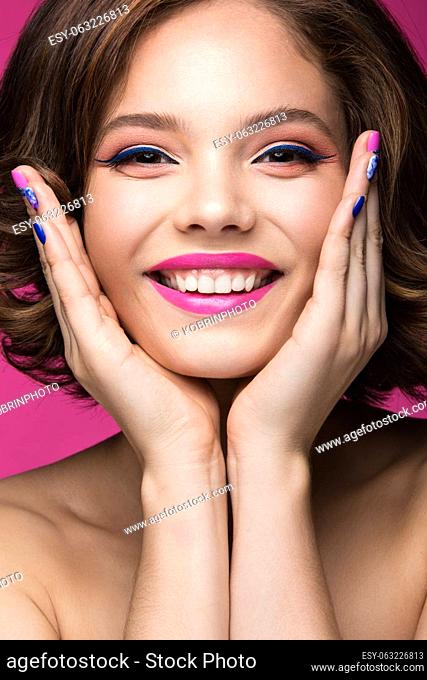 Beautiful model girl with bright makeup, smile and colored nail polish. Beauty face. Short colorful nails. Picture taken in the studio on a pink background