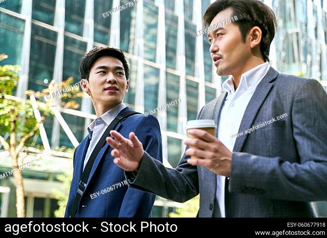 side view of two asian corporate executives discussing business while walking in street in downtown of modern city