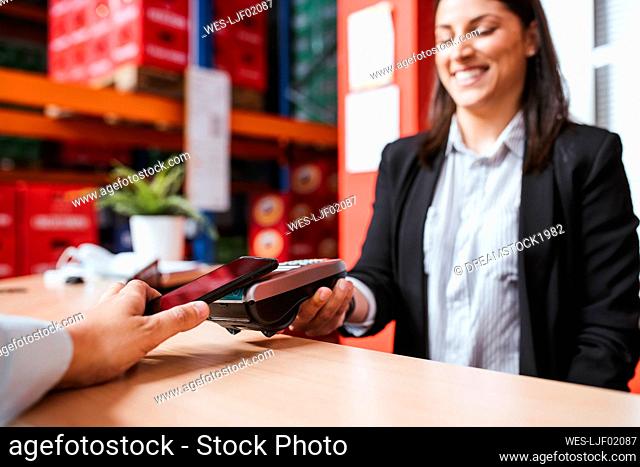 Smiling female manager holding card reader for customer with smart phone