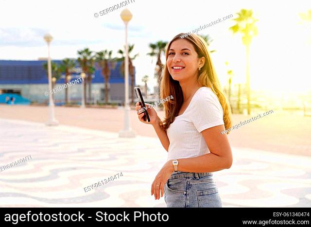 Millennial girl walking alone holding smartphone at sunset