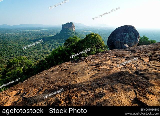 Big Stone on sunny orange Pidurangala Rock with view on Lions Rock surrounded by forest in Sigiriya, Sri Lanka