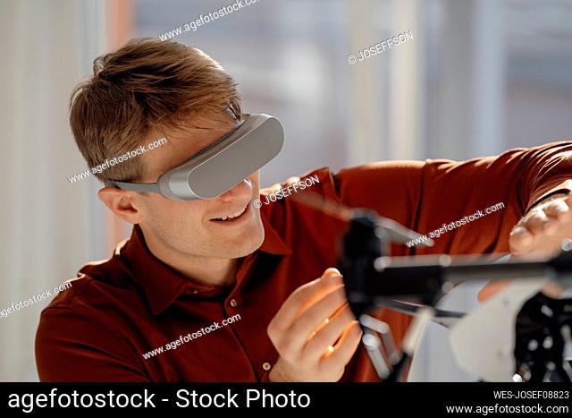 Smiling businessman wearing virtual reality simulator gesturing towards drone in office