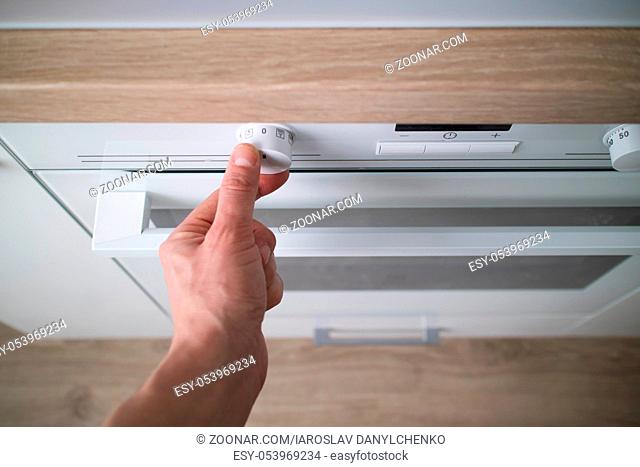 Household kitchen scene of a man hand turning on a white electric oven in the kitchen. Selecting or setting the temperature in a modern oven