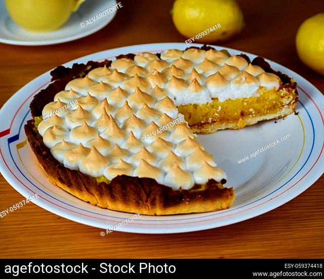 Lemon Pie with merengue without one slice in a dish decorated with two lemons and a cup of coffee