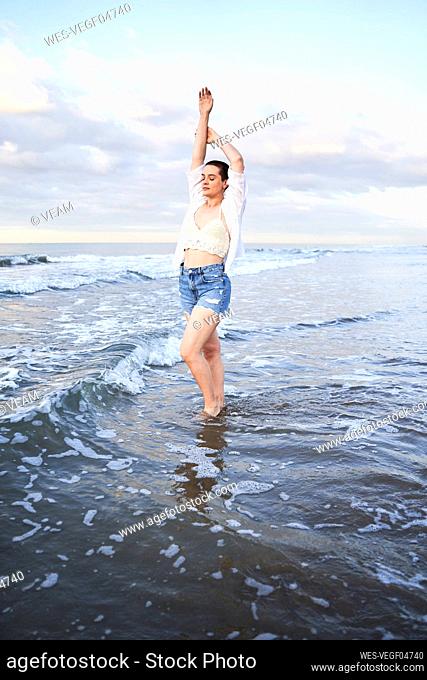 Young woman standing with hands raised in water
