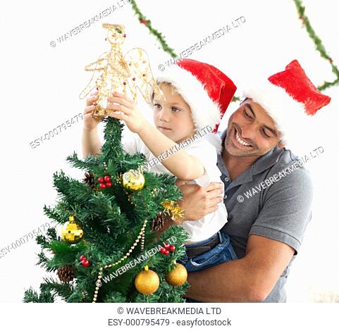 Happy father helping his son to put an angel on the Christmas tree at home