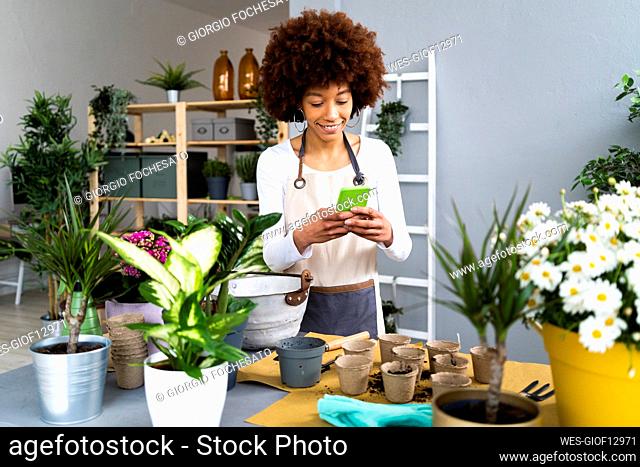Smiling female florist using mobile phone while standing by table at plant shop